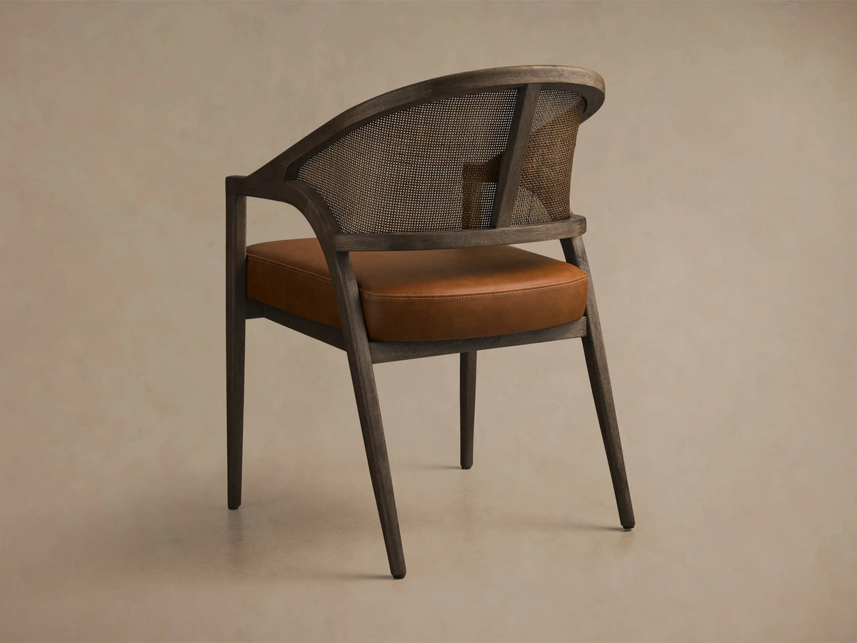 Rear view of the Aimee Faux Leather Dining Arm Chair with a black drifted solid oak frame, rattan cane back, and brown faux leather seat.