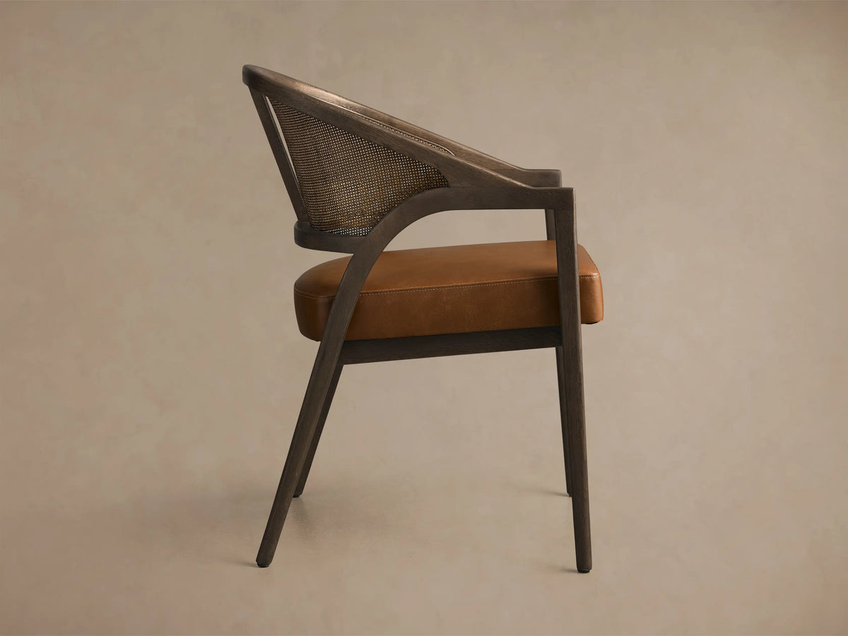 Front view of an Aimee Faux Leather Dining Arm Chair with a dark wood frame, natural rattan back, and brown faux leather seat.