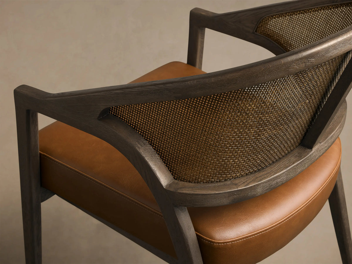 Side view of Aimee Faux Leather Dining Arm Chair with a dark wood frame, cane back, and brown faux leather seat.