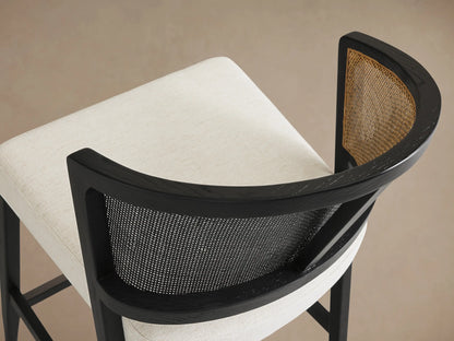 Aimee Armless Counter Stool with solid black oak frame, rattan cane back, and white upholstered seat on a neutral background.