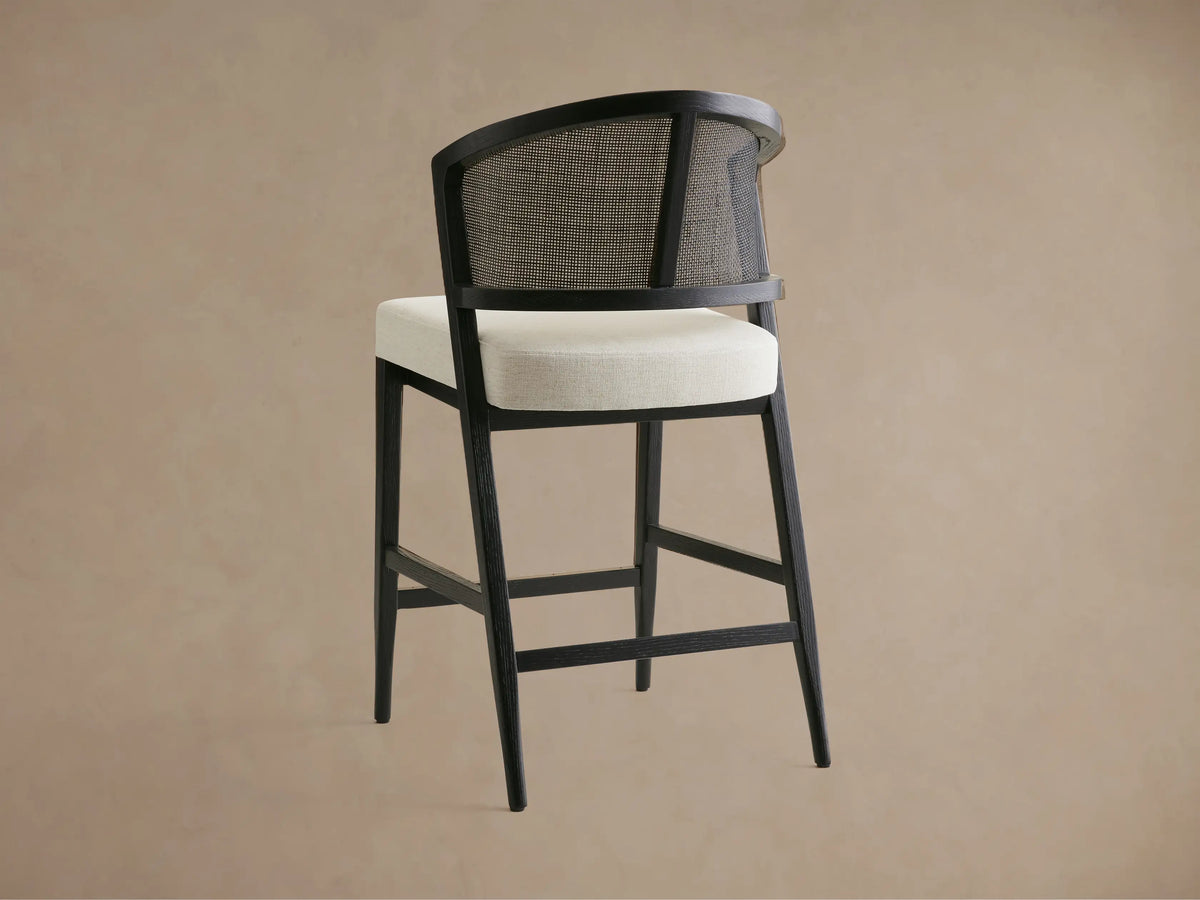 Aimee Armless Counter Stool with curved wooden back, rattan cane, and upholstered seat in cream, viewed from above at an angle.