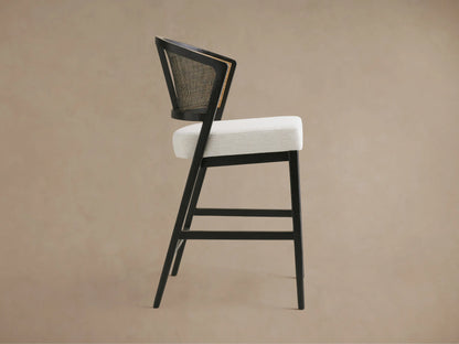 Aimee Armless Counter Stool with a solid oak frame, rattan cane back, and upholstered seat in a light fabric, shown from the back.