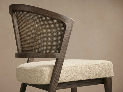 Aimee Armless Counter Stool, front view. Dark oak frame, rattan cane back, ivory upholstered seat. Set on wooden floor.