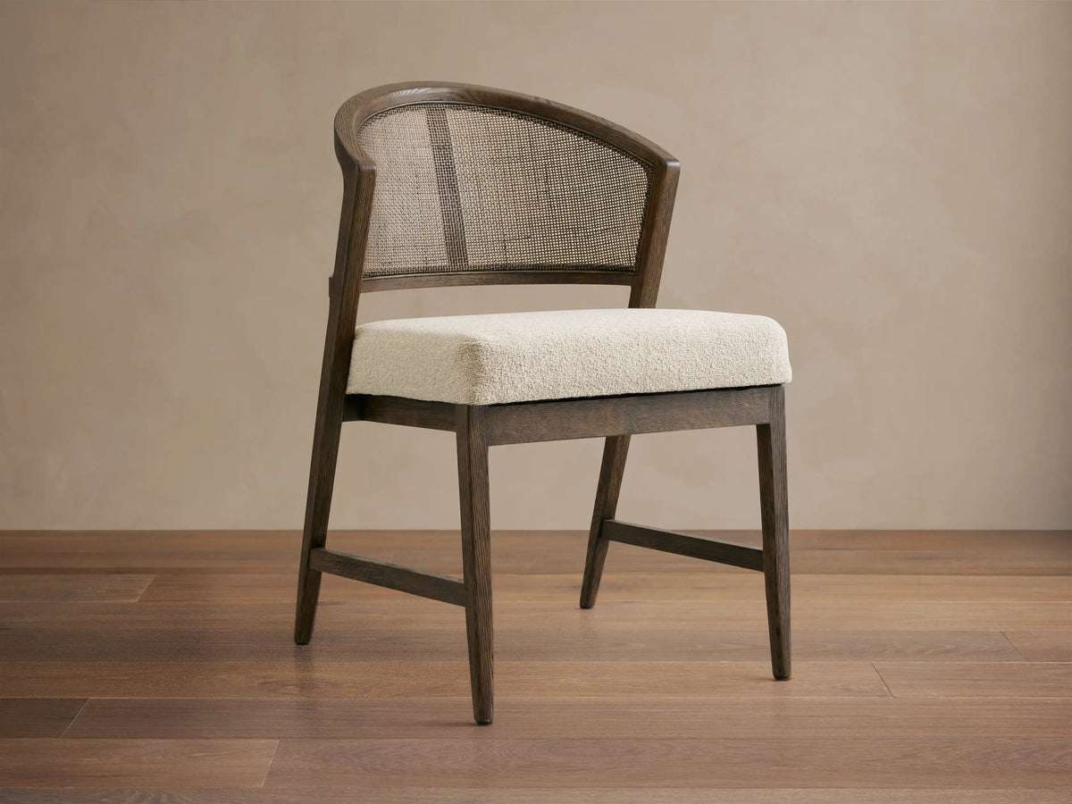 Aimee Dining Side Chair with dark wood frame, rattan cane back, and cream upholstered seat on wooden floor.