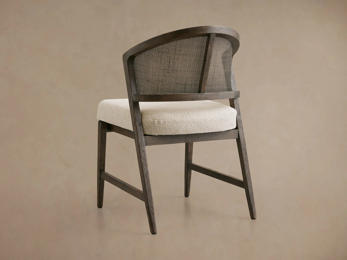Aimee Dining Side Chair with a curved oak frame, rattan cane back, and light upholstered cushion seat on a beige background.