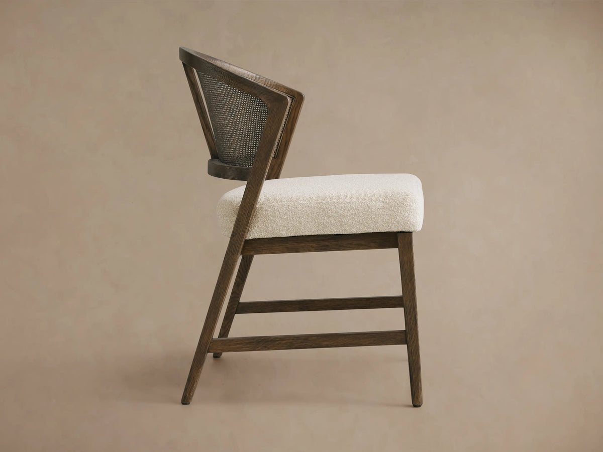 Aimee Dining Side Chair with solid oak frame, black driftwood finish, rattan cane back, and cushioned beige seat, viewed from the side.
