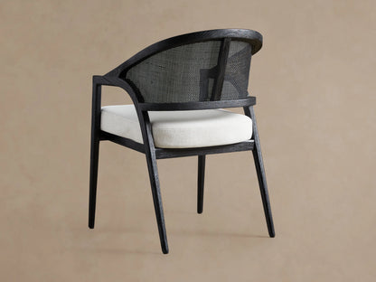 Aimee Dining Arm Chair with a black drifted oak frame, rattan cane back, and light upholstered cushion, viewed from the side.