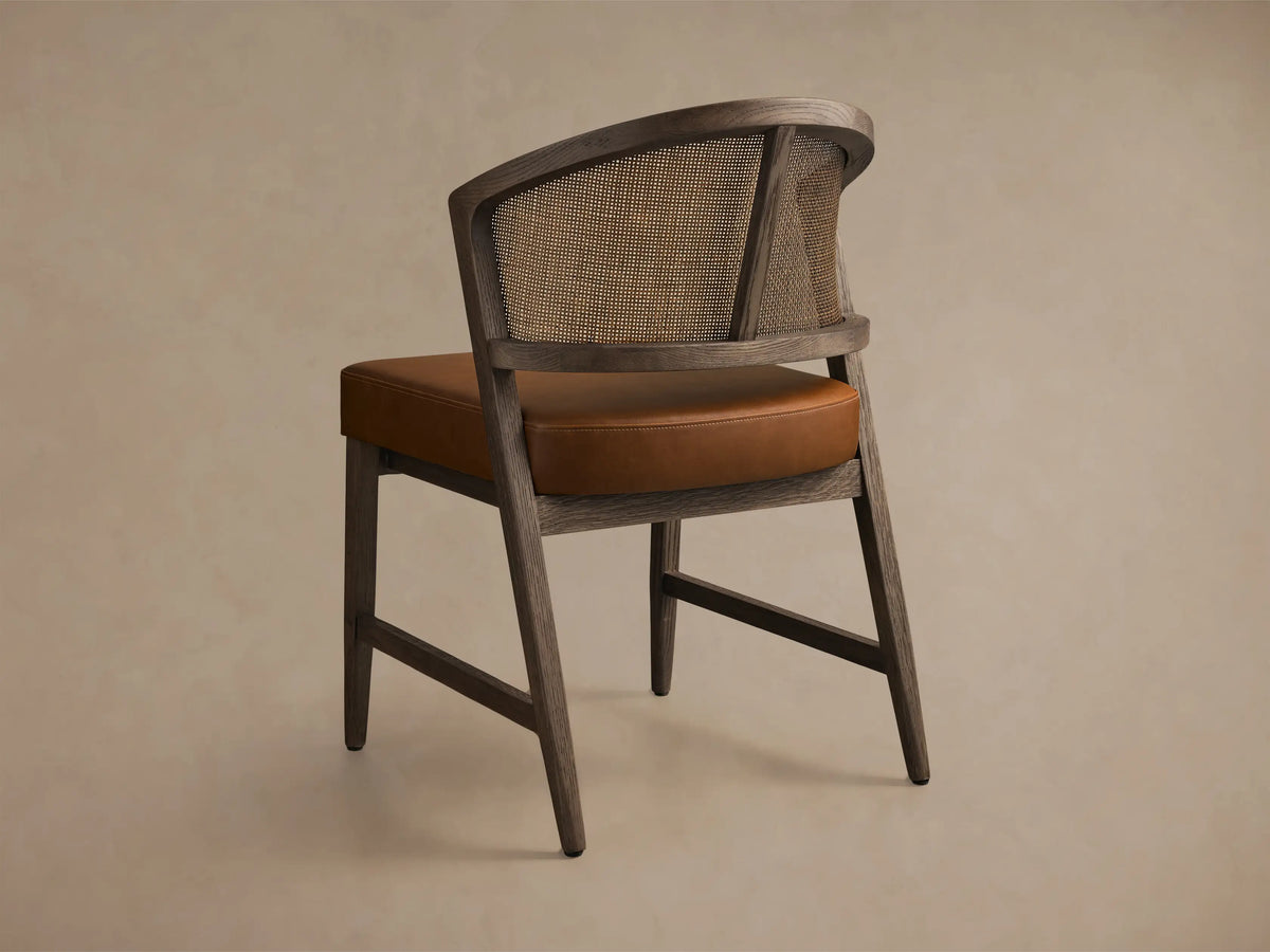 Angled rear view of the Black Drifted Aimee Faux Leather Dining Side Chair, with a rattan cane back and brown faux leather seat.