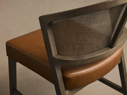 Front angled view of the Black Drifted Aimee Faux Leather Dining Side Chair with a rattan cane back and brown faux leather seat.