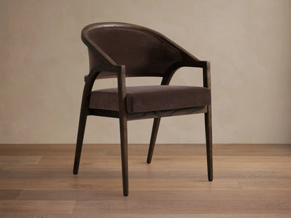 Aimee Upholstered Back Dining Arm Chair in dark brown fabric with solid oak frame, curved back, and cushioned seat on wooden floor.