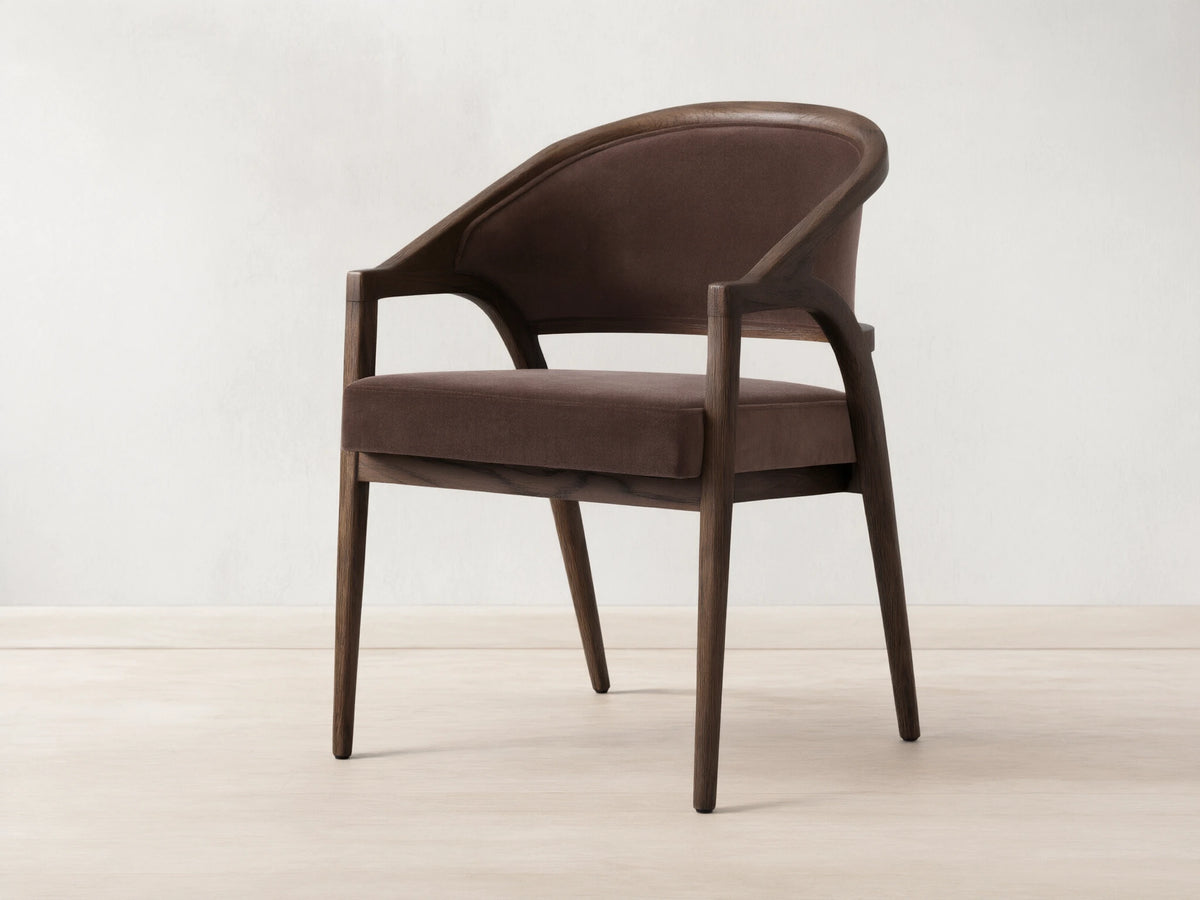 Aimee Upholstered Back Dining Arm Chair in dark brown fabric with solid oak frame, curved back, and cushioned seat on wooden floor.
