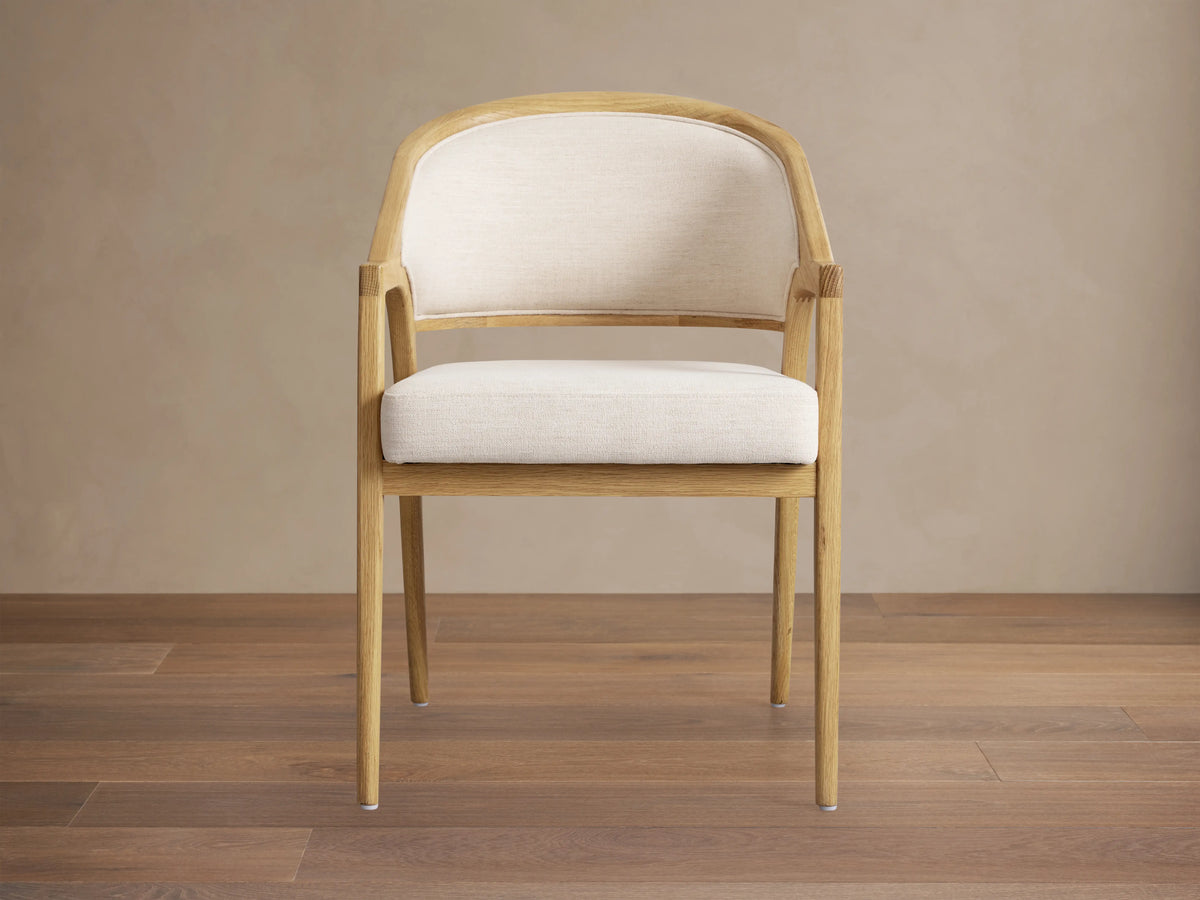 Aimee Upholstered Back Dining Arm Chair in light beige fabric with curved solid oak frame, hand-finished with a subtle sheen.