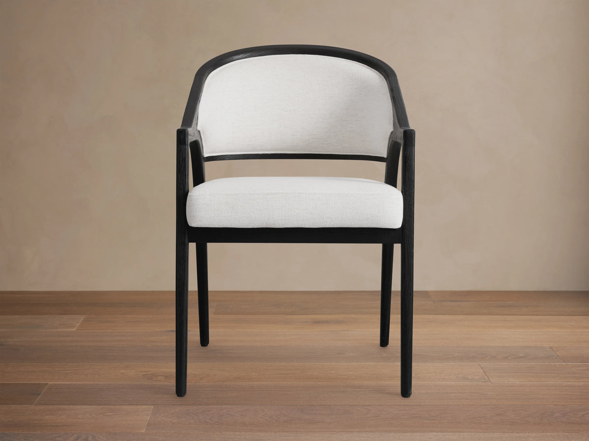 Angled view of Black Drifted Aimee Upholstered Back Dining Arm Chair with dark wood frame and upholstered seat, at a table.