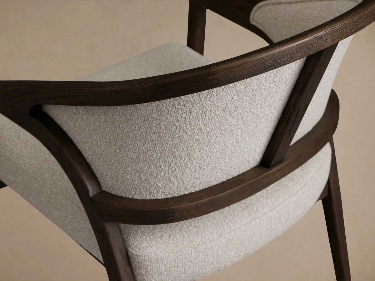 Aimee Upholstered Back Dining Arm Chair in a neutral fabric, with a curved oak frame, hand-finished with lacquer, on a wood floor.