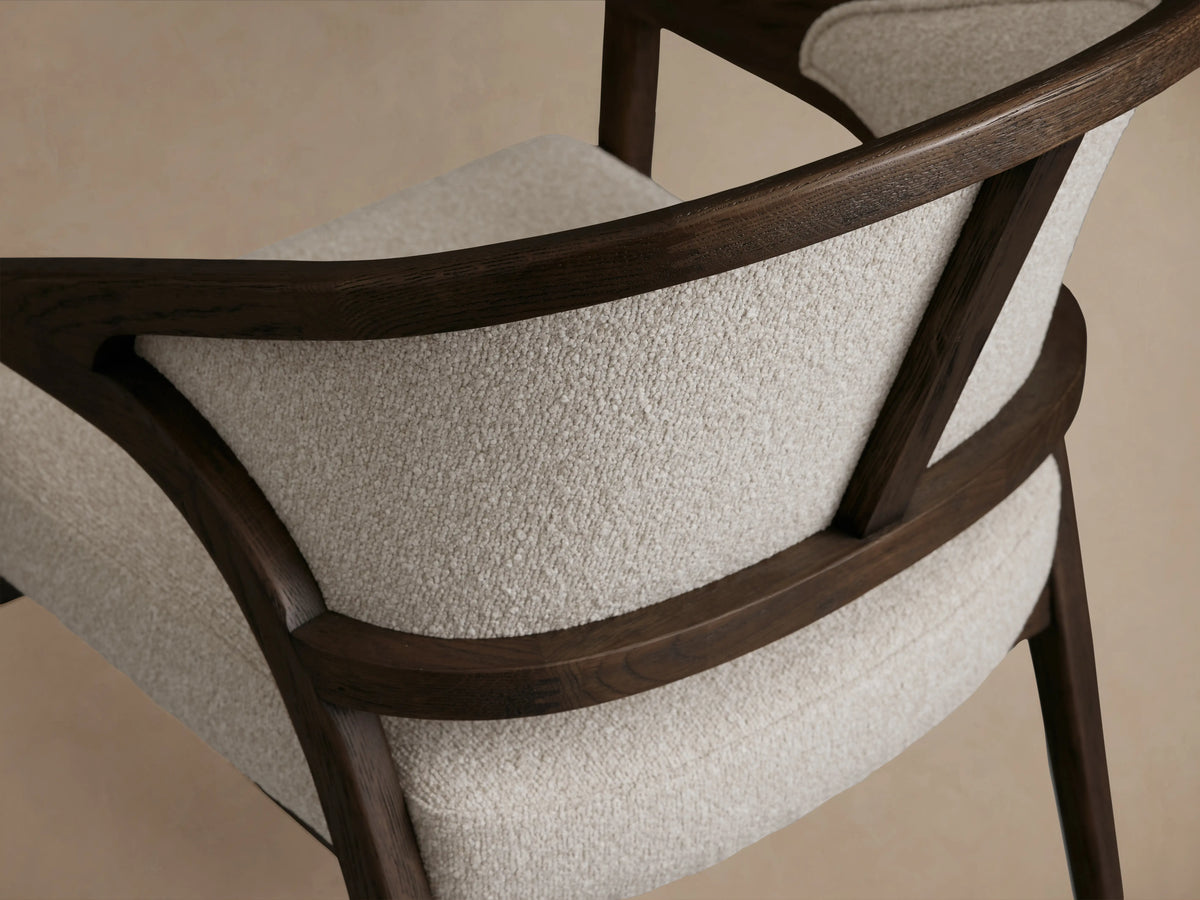 Aimee Upholstered Back Dining Arm Chair with a dark wooden frame, cream upholstered back and seat, on a wooden floor.
