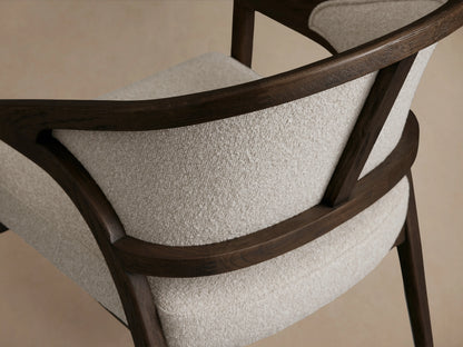 Aimee Upholstered Back Dining Arm Chair with a dark wooden frame, cream upholstered back and seat, on a wooden floor.