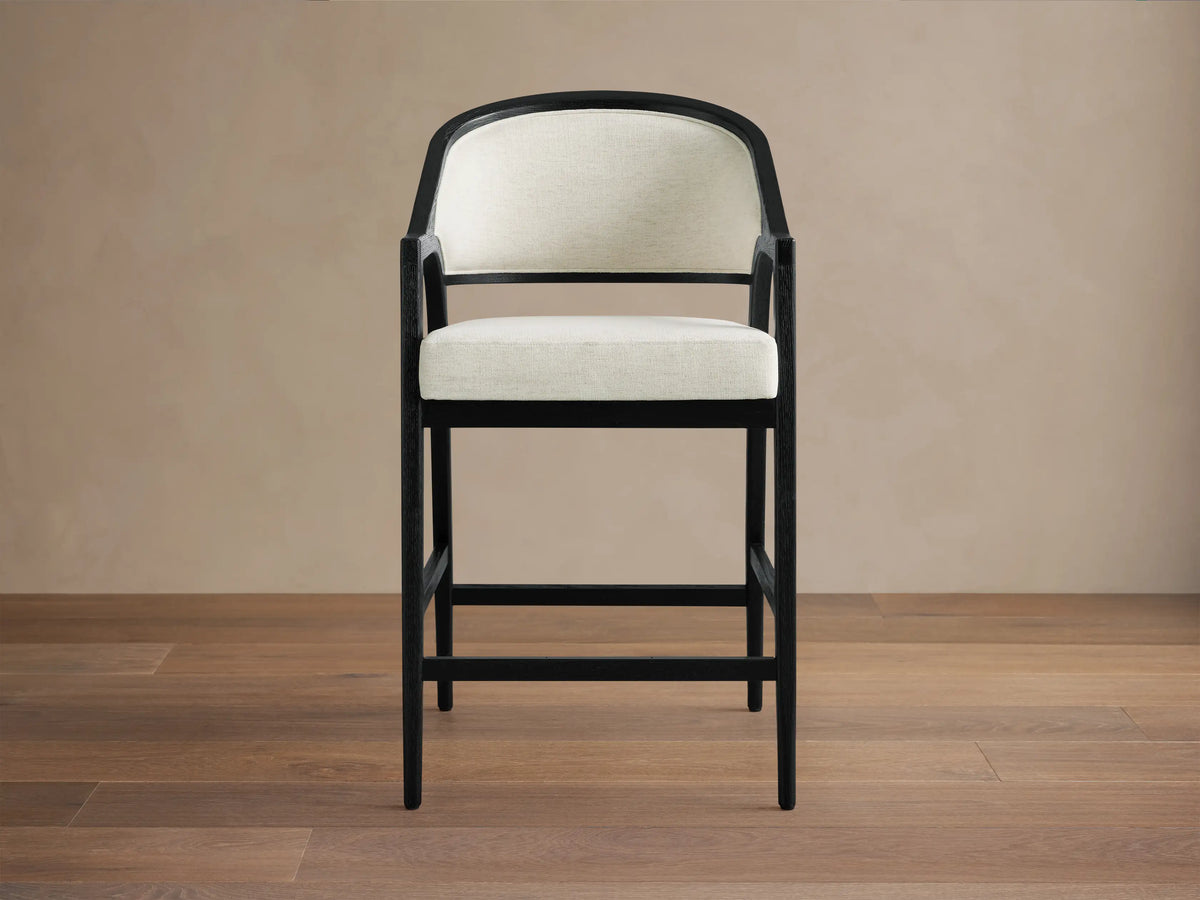 Aimee Upholstered Back Counter Stool with solid oak frame, black lacquer finish, cream upholstered back and seat, on wooden floor.