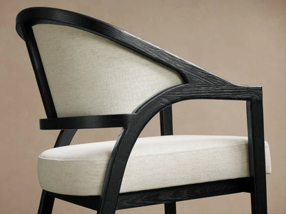 Aimee Upholstered Back Counter Stool with a black oak frame, beige fabric seat and backrest on a wooden floor background.