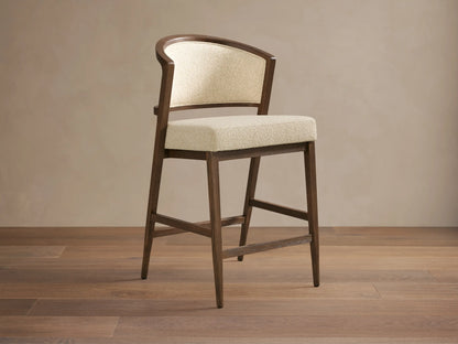 Aimee Upholstered Back Armless Counter Stool with a cream upholstered seat and back, solid oak frame, on a wooden floor.
