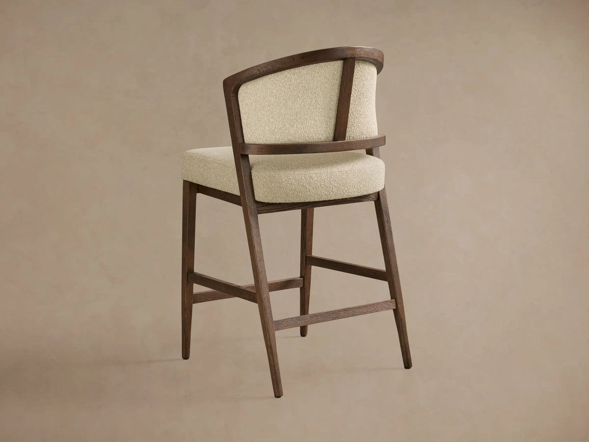 Aimee Upholstered Back Armless Counter Stool featured with a solid oak frame and light textured fabric, showcasing its curved backrest.