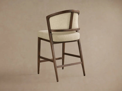 Aimee Upholstered Back Armless Counter Stool featured with a solid oak frame and light textured fabric, showcasing its curved backrest.