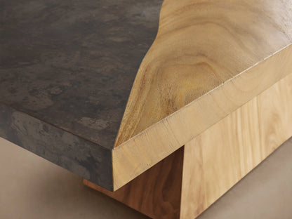 Almeria Dining Table with a thick, rectangular guanacaste wood top and oxidized steel panel on a trapezoidal wooden base.