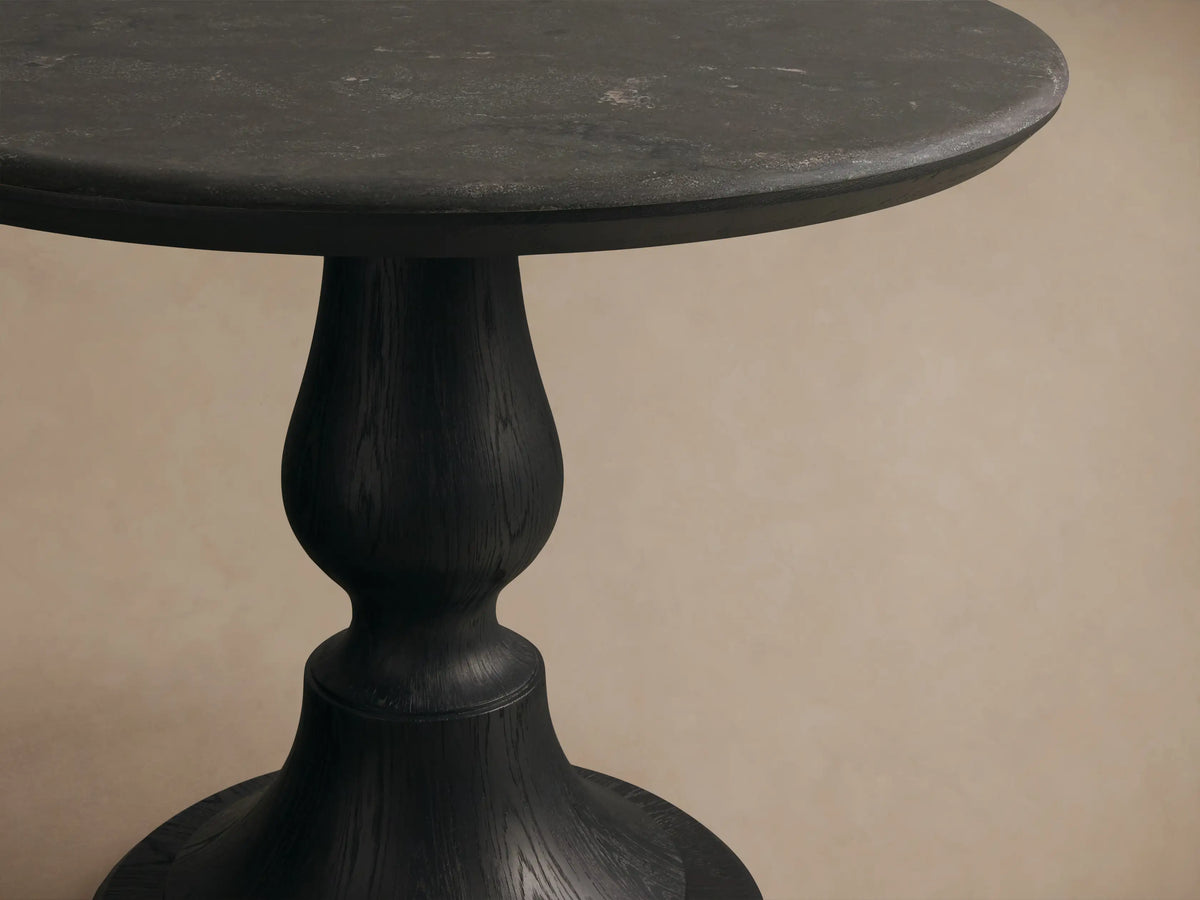 Amelia Bistro Table featuring a dark bluestone round top and a black sculpted oak pedestal base, set on a wood floor.