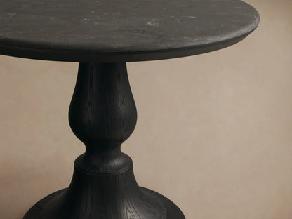 Amelia Bistro Table featuring a dark bluestone round top and a black sculpted oak pedestal base, set on a wood floor.