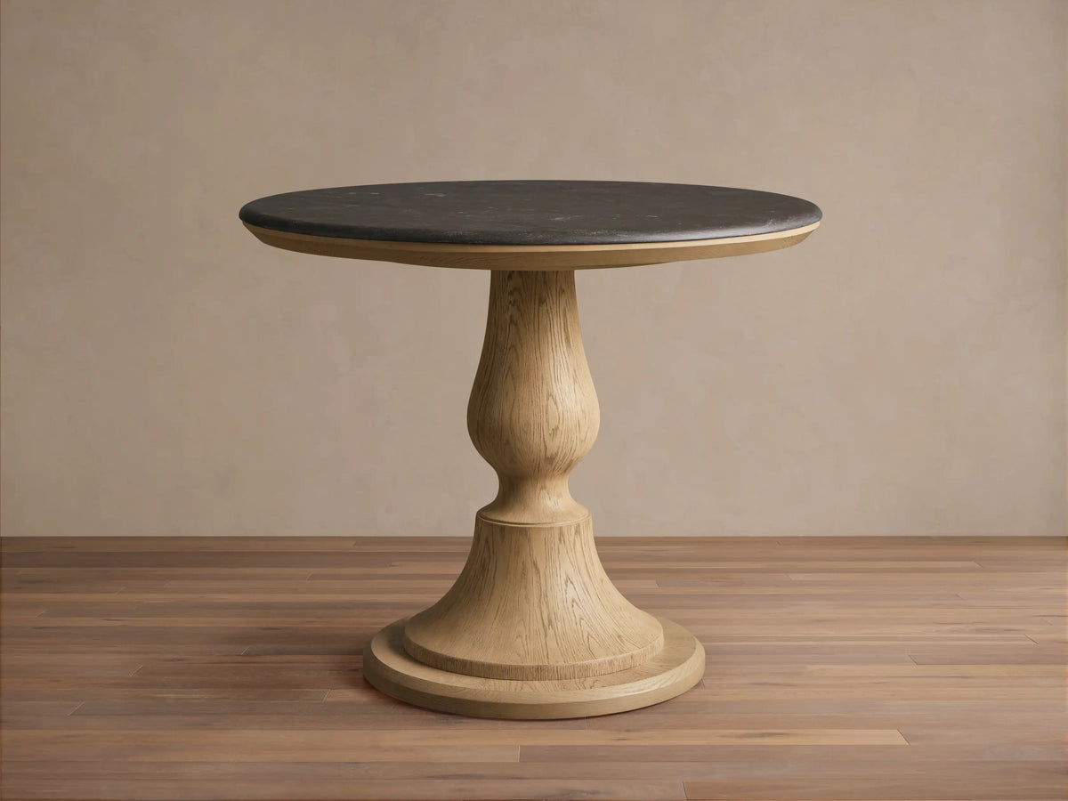 Round Amelia Bistro Table featuring a dark bluestone top and a light oak wood pedestal base, standing on a wooden floor.