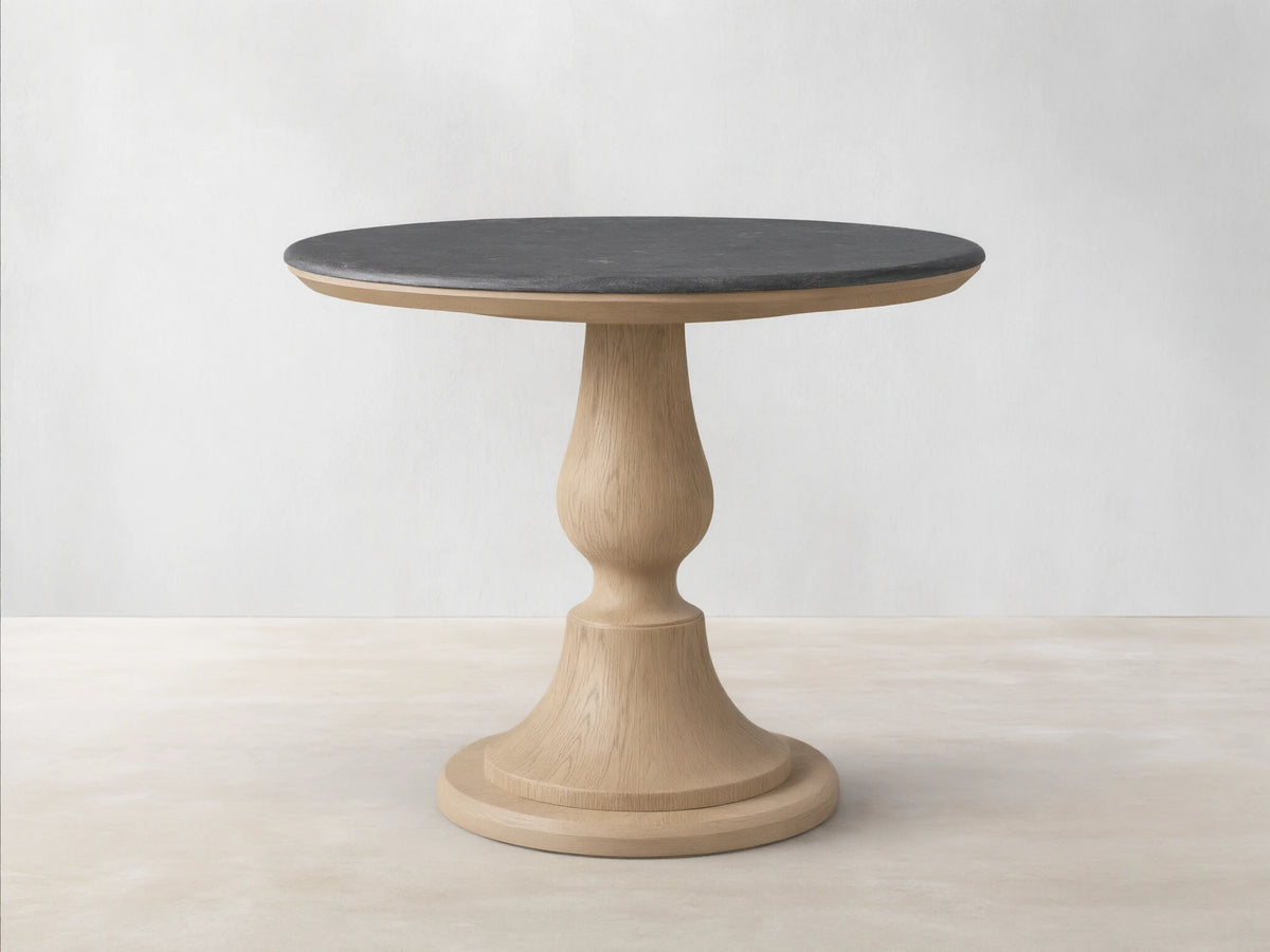 Round Amelia Bistro Table featuring a dark bluestone top and a light oak wood pedestal base, standing on a wooden floor.