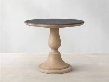 Round Amelia Bistro Table featuring a dark bluestone top and a light oak wood pedestal base, standing on a wooden floor.
