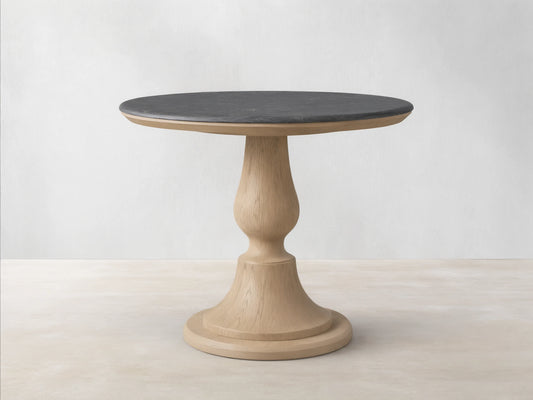 Round Amelia Bistro Table featuring a dark bluestone top and a light oak wood pedestal base, standing on a wooden floor.