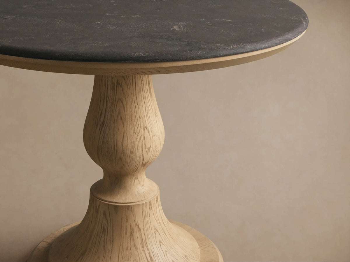Round Amelia Bistro Table featuring a dark bluestone top and a light oak wood pedestal base, standing on a wooden floor.