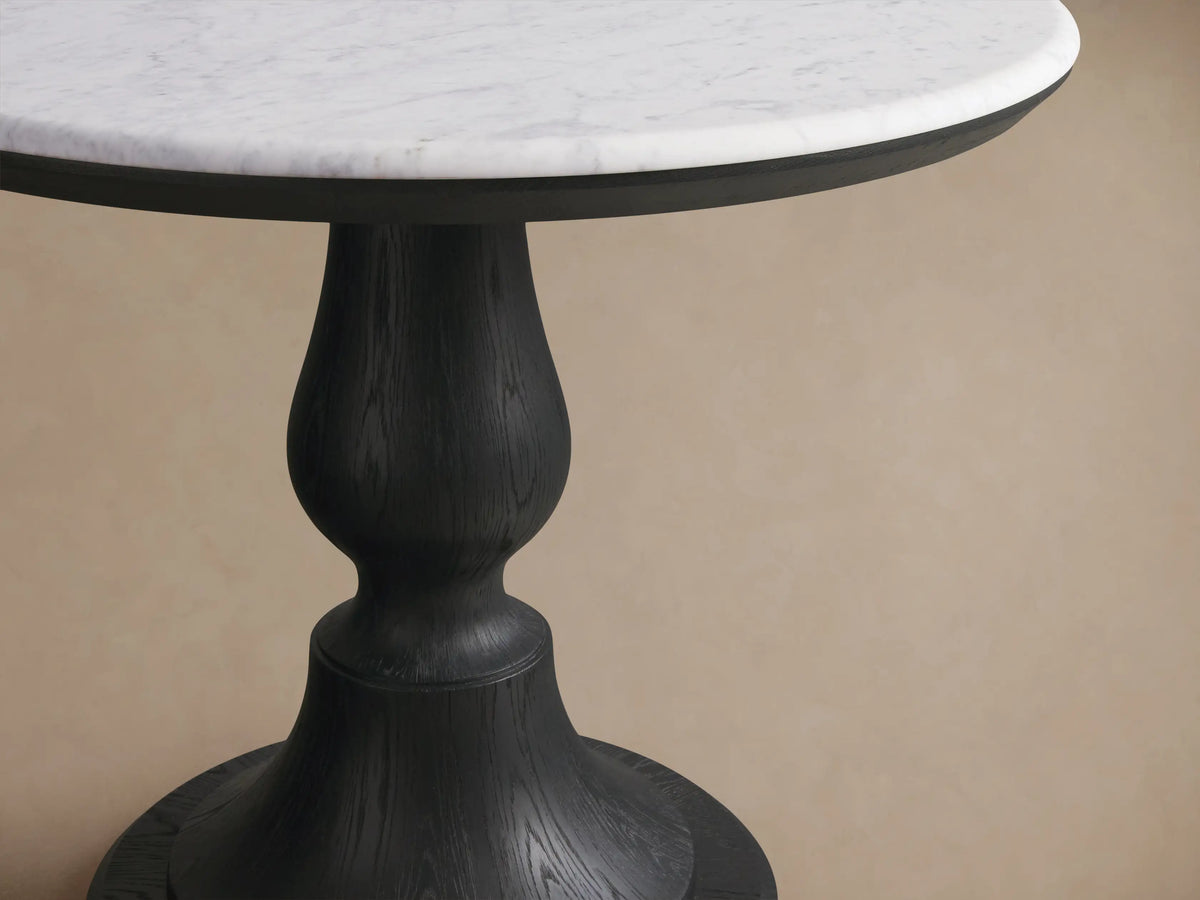 Amelia Bistro Table: Round white marble top on a dark, sculpted pedestal base with visible wood grain.