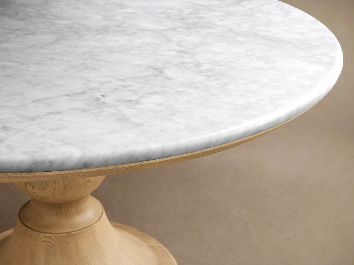 Round Amelia Dining Table with a white marble top and a beige oak grain pedestal base in a sunny dining nook.