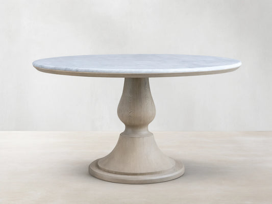 Amelia Dining Table: Round white marble top with gray veins, light oak pedestal base with visible wood grain, on wood floor.