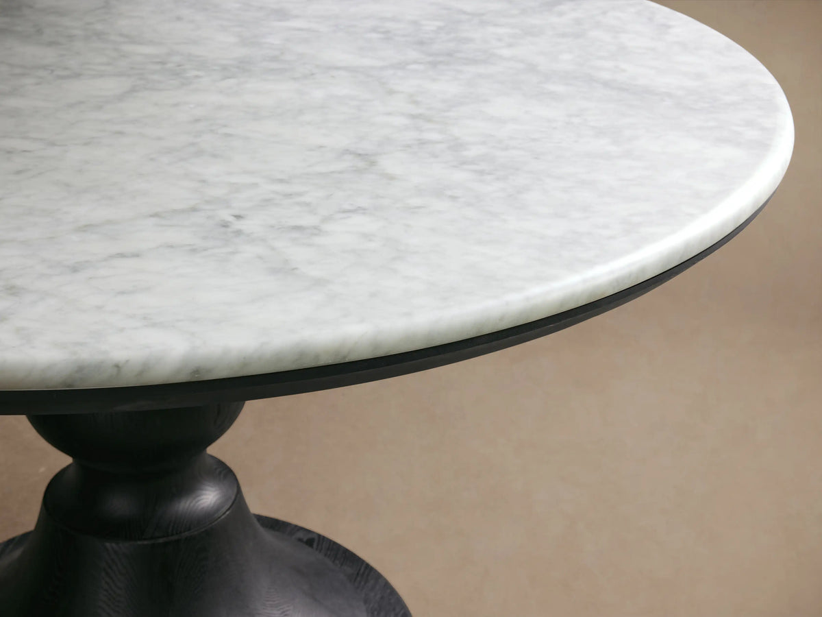 Amelia Dining Table with a light bluestone top and oak grain pedestal base, set in a sunny dining nook with a striped banquette.