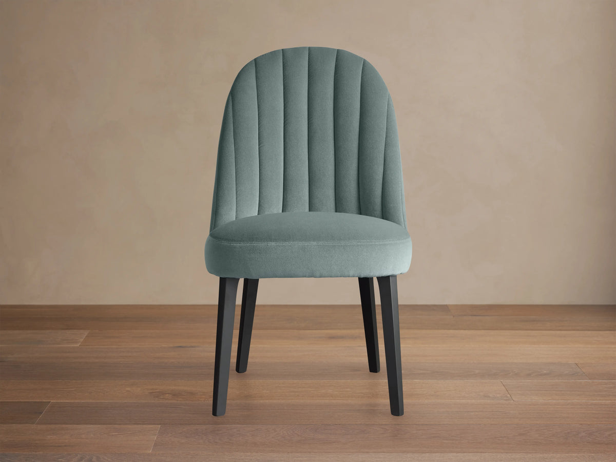 Arco Channel Dining Chair with teal upholstery and vertical channel detailing on backrest, dark wood legs, on wooden floor.