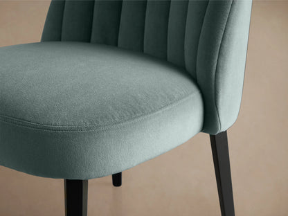 Arco Channel Dining Chair with teal upholstered, channel-detailed backrest, padded seat, and dark wooden legs on a wooden floor.