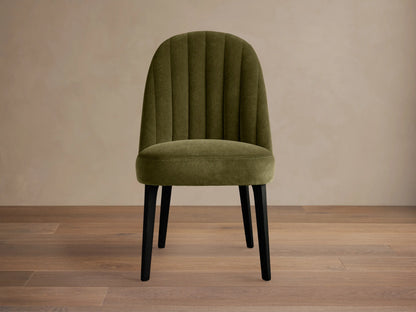 Arco Channel Dining Chair, olive green velvet with curved, channel-tufted back and black legs, angled on wood floor.