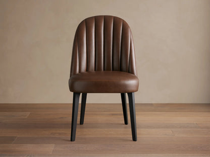 Arco Faux Leather Dining Chair: Brown, channel-tufted curved back, dark legs. Centered on a wooden floor.