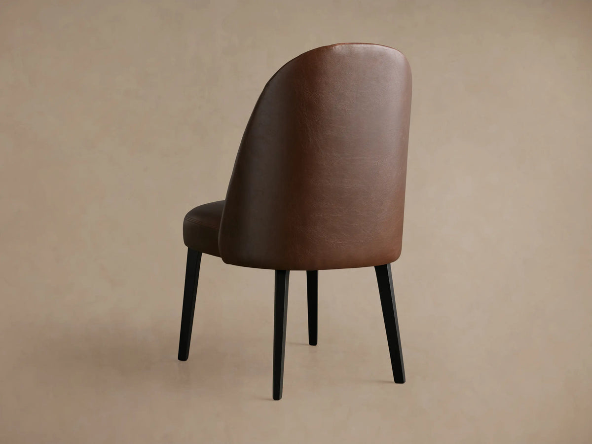 Close-up of Arco Faux Leather Dining Chair's backrest, showing rich brown faux leather with elegant channel detailing.