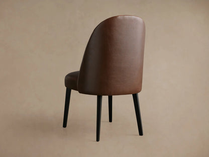 Close-up of Arco Faux Leather Dining Chair's backrest, showing rich brown faux leather with elegant channel detailing.