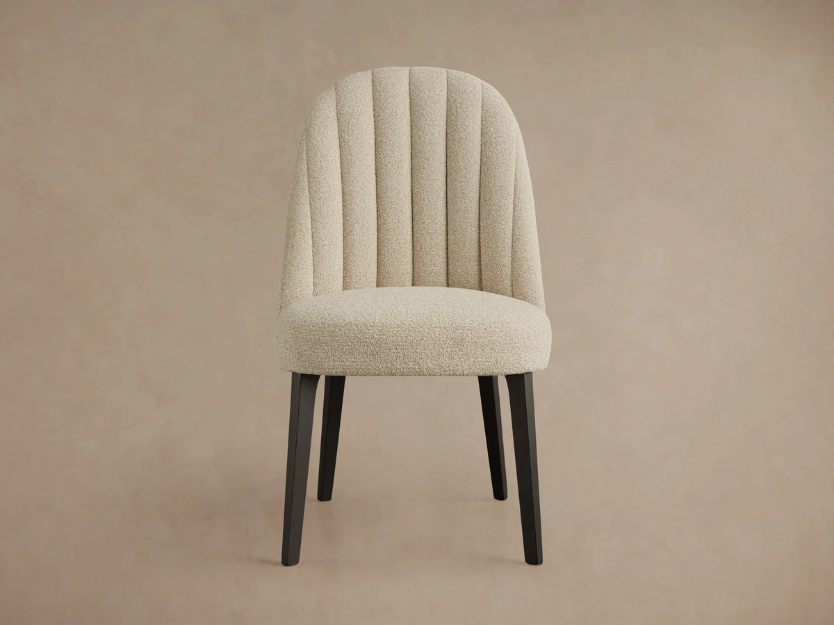 Arco Channel Dining Chair, cream boucle fabric with a curved channel-tufted backrest and dark wood legs, angled right.
