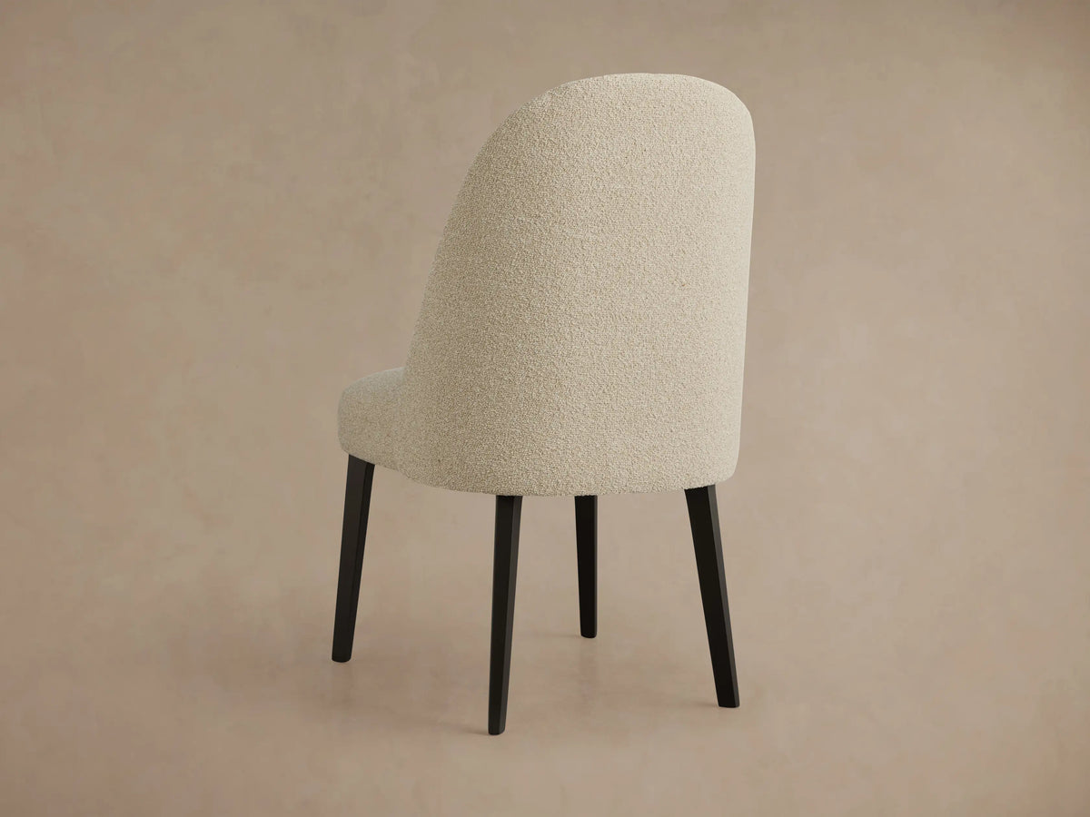 Close-up of Arco Channel Dining Chair. Light beige textured upholstery with channel detailing on the curved backrest, black leg.
