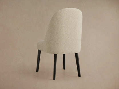 Close-up of Arco Channel Dining Chair. Light beige textured upholstery with channel detailing on the curved backrest, black leg.