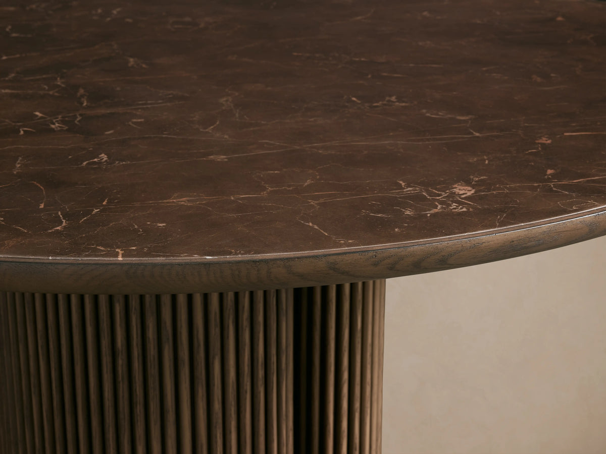 Astor Round Dining Table with dark oak veneer top, dual cylindrical reeded oak bases, on light wood floor, against neutral wall.