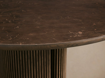 Astor Round Dining Table with dark oak veneer top, dual cylindrical reeded oak bases, on light wood floor, against neutral wall.