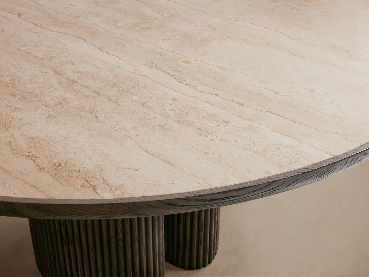Astor Round Dining Table with light marble top and dark reeded oak cylindrical base on a wooden floor.
