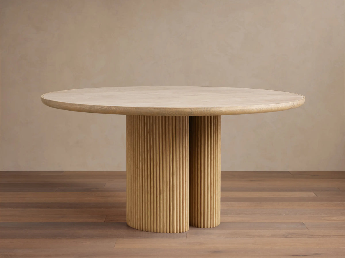 Astor Round Dining Table with light oak wood top and two reeded cylindrical bases, standing on a wood floor.